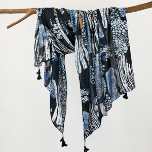 May include: A black and blue patterned scarf with tassels. The scarf has a geometric and abstract design.