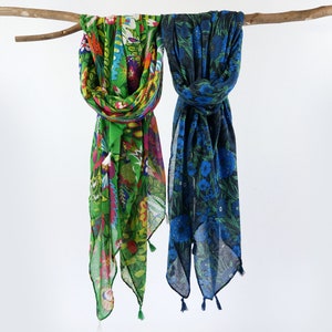 Puede incluir: Dos bufandas coloridas con estampados florales colgando de una rama. Una bufanda es verde con flores rosas, azules y amarillas. La otra bufanda es azul con flores blancas.