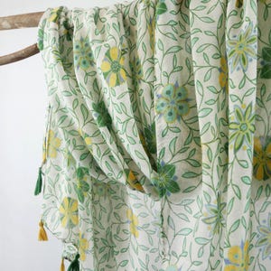 May include: A white sheer scarf with a green floral pattern and yellow tassels. The scarf is made of a lightweight fabric and is perfect for adding a touch of color to any outfit.