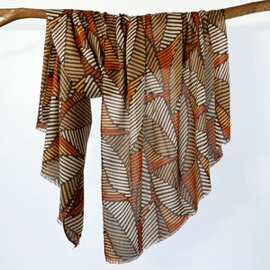 May include: A brown, orange, and white patterned scarf with a geometric design. The scarf is draped over a branch.