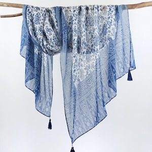 May include: A blue and white patterned scarf with tassels hanging from the bottom corners. The scarf is draped over a branch.