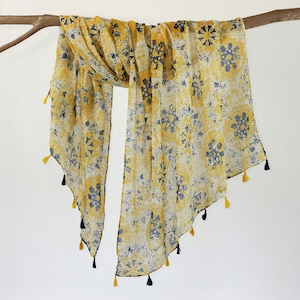 May include: A yellow and blue patterned scarf with tassels. The scarf is made of a sheer fabric and has a geometric design.