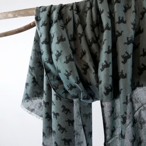 May include: A teal blue scarf with a repeating pattern of black horses. The scarf is draped over a branch.