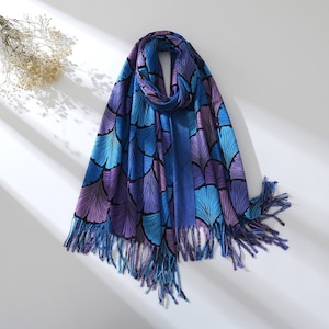 May include: A blue and purple scarf with a leaf pattern and fringe. The scarf is folded in half and has a tassel on each end.