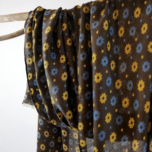 May include: Brown fabric with a repeating pattern of yellow and blue flowers. The fabric is folded and draped over a branch.