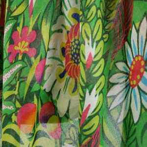 Puede incluir: Tela verde con estampado floral con flores blancas, rojas, amarillas y azules. La tela es transparente y tiene una superficie texturizada.