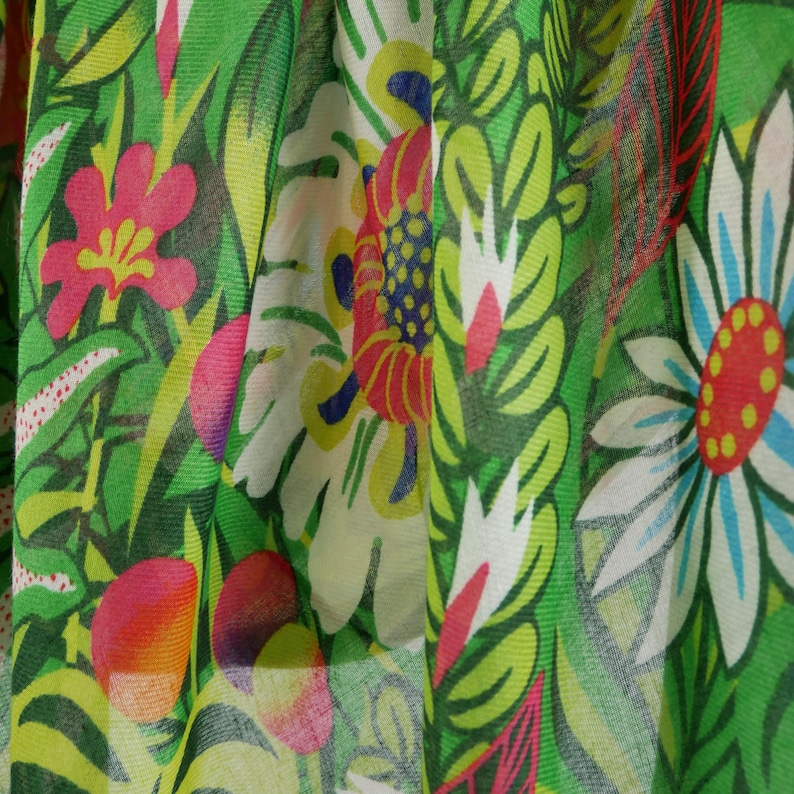 Puede incluir: Tela verde con estampado floral con flores blancas, rojas, amarillas y azules. La tela es transparente y tiene una superficie texturizada.