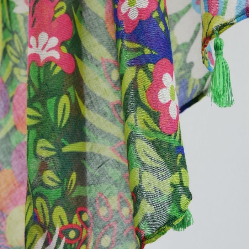 Puede incluir: Una bufanda de color verde, rosa y azul con estampado floral y un borla verde en el extremo.