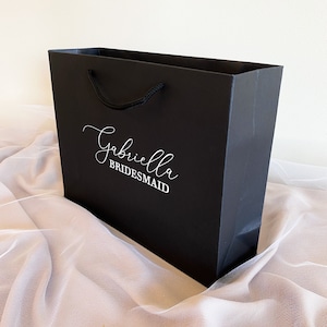 May include: Black gift bag with a white handle and the text "Gabriella Bridesmaid" printed on the front.