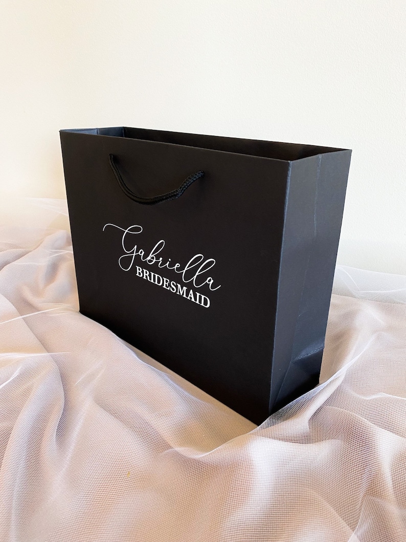 May include: Black gift bag with a white handle and the text "Gabriella Bridesmaid" printed on the front.