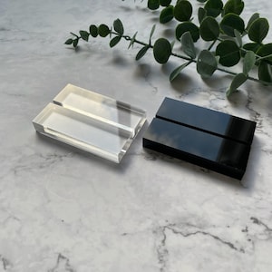 May include: Two acrylic display stands, one clear and one black. Both stands have two slots for displaying items.
