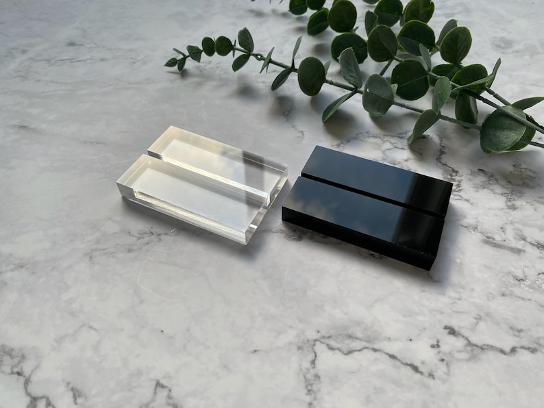 May include: Two acrylic display stands, one clear and one black. Both stands have two slots for displaying items.