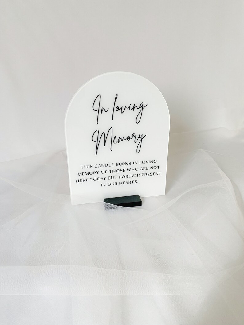 以下が含まれることがあります： 「In loving memory」というテキストが書かれた白いアクリル製のアーチと、その下に「This candle burns in loving memory of those who are not here today but forever present in our hearts.」というテキストが書かれた小さなテキストブロックがあります。