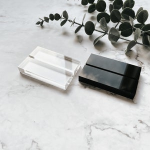 K&ouml;nnte beinhalten: Zwei Acryl-Pr&auml;sentationsst&auml;nder, einer transparent und einer schwarz, zum Pr&auml;sentieren von Visitenkarten oder anderen kleinen Gegenst&auml;nden.
