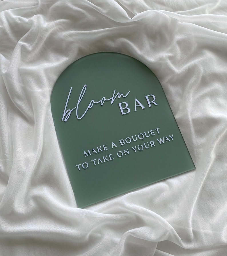 May include: A green arch-shaped sign with white text that reads "bloom BAR" and "MAKE A BOUQUET TO TAKE ON YOUR WAY".