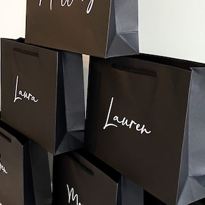 May include: A stack of black gift bags with white lettering. The names "Laura", "Lauren", "Ben", and "Mary" are written on the bags.