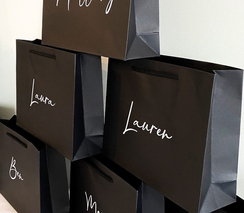 May include: A stack of black gift bags with white lettering. The names "Laura", "Lauren", "Ben", and "Mary" are written on the bags.