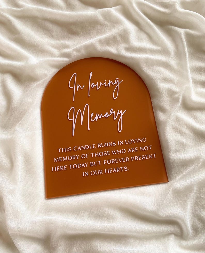 以下が含まれることがあります： 「In loving memory. This candle burns in loving memory of those who are not here today but forever present in our hearts.」と書かれた白い文字が、茶色のアーチ型のプレートに入っています。