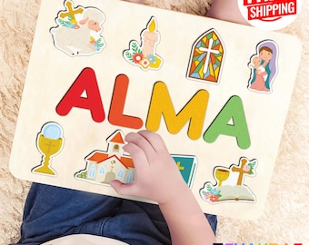 May include: A personalized wooden puzzle featuring the name "ALMA" in colorful letters. The puzzle includes various religious symbols such as a cross, a church, a chalice, a candle, a lamb, a bible, and a depiction of Mary and Jesus.