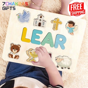 May include: A wooden puzzle with the name "LEAR" spelled out in colorful letters. The puzzle includes various religious images, such as a dove, a church, a cross, a lamb, a chalice, and a child holding a teddy bear. The puzzle is designed for children to learn the alphabet and religious symbols.