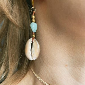 Könnte beinhalten: Einzelner goldener Creolen-Ohrring mit hängendem Design. Der Ohrring hat eine natürliche Muschel, einen hellblauen Stein und goldfarbene Perlen. Der Ohrring ist an einem goldenen Reifen befestigt.