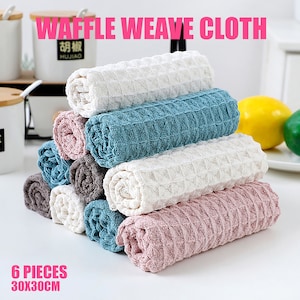 May include: Six waffle weave kitchen cloths in various colors, including white, blue, pink, and gray. The cloths are rolled up and stacked on top of each other. The text "6 PIECES 30X30CM" is printed below the stack of cloths.