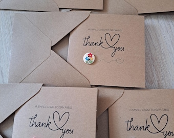May include: Five brown kraft paper cards with envelopes, each featuring the black printed text A SMALL CARD TO SAY A BIG thank you and a heart icon. Each card displays a unique decorative button: leopard print, green heart, floral, pink heart, and floral.