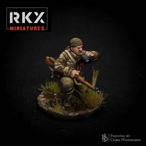 Könnte beinhalten: Miniaturfigur eines Soldaten in Tarnkleidung, der kniet und aus einem Becher trinkt. Die Figur hält ein Gewehr und steht auf einer kleinen, grasbewachsenen Basis. Das Bild enthält den Text "RKX MINIATURES".