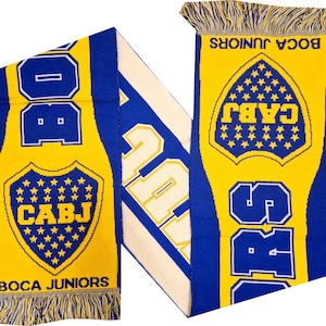 Pode incluir: Cachecol azul e amarelo do Boca Juniors com o logotipo e o texto da equipa. O cachecol tem um escudo com estrelas e as letras CABJ. O texto "BOCA JUNIORS" também é visível. O cachecol tem franjas em ambas as extremidades.