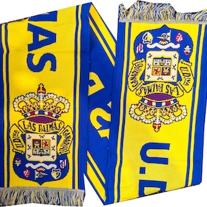 Op de afbeelding: Een gele en blauwe gebreide sjaal met de tekst "LAS PALMAS" en "U.D." en een wapen. De sjaal heeft een gefranjerde rand en is waarschijnlijk een fanartikel.