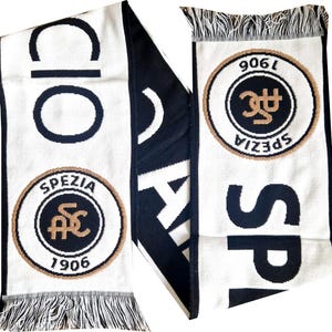 May include: A white and black scarf with the word "CIO" and "SPEZIA" in large black letters. The scarf features a circular emblem with "SPEZIA" and "1906" in a gold border. Fringes are at the ends.