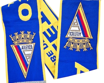May include: A blue and yellow scarf with the word "ATLETICO" and a team logo. The scarf has a fringe at the ends. The team logo is a triangle with red, yellow, and white stripes.
