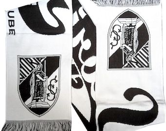 May include: White and black knitted scarf with fringe. The scarf features a shield with a figure and text, along with other graphic designs and text. The scarf is made of a soft material and is suitable for cold weather.