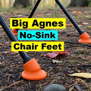 Puede incluir: Primer plano de patas de silla negras con patas de silla naranjas No-Sink. El texto "Big Agnes No-Sink Chair Feet" se muestra en cuadros amarillos y azules. El suelo está cubierto de hojas y agujas de pino.
