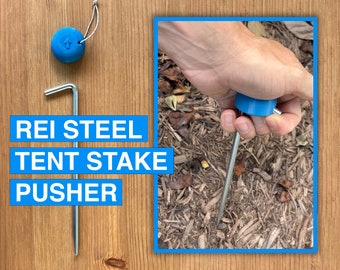 May include: A blue tent stake pusher with a metal stake and a blue handle. The text "REI STEEL TENT STAKE PUSHER" is printed on a blue background.