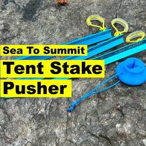 May include: Camping equipment set, featuring blue tent pegs, yellow pullers, and a blue stake pusher. The image includes the text "Sea To Summit Tent Stake Pusher" in yellow and black.