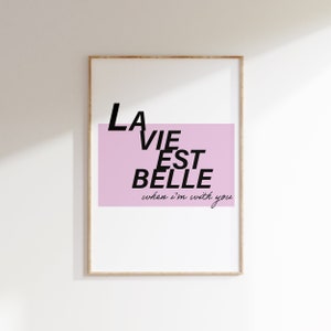 May include: Framed art print with the phrase "LA VIE EST BELLE" in black text, set against a light pink rectangular background. The words "when I'm with you" are written below in a script font.