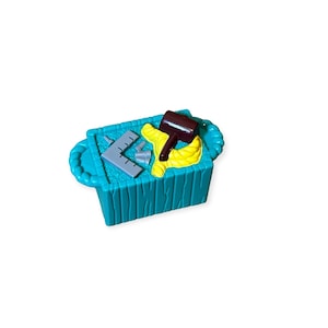 May include: A teal blue plastic toy toolbox with a yellow rope, a brown hammer, and a gray protractor inside.