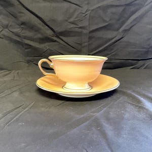 May include: A pink teacup and saucer set with gold trim. The cup has a rounded shape and a small handle. The saucer is a matching color and has a gold rim.