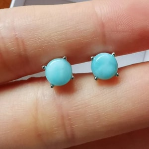 May include: A pair of silver stud earrings with round, light blue gemstones.