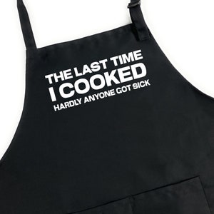 May include: Black apron with white text that reads "The last time I cooked hardly anyone got sick."