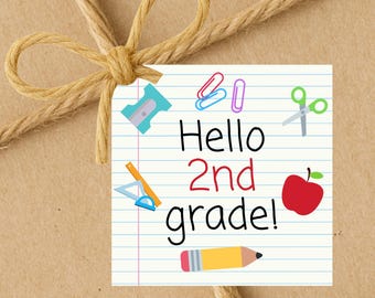May include: A square tag with the text "Hello 2nd grade!" and school-themed illustrations, including a pencil, apple, scissors, and paper clips. The tag is tied with twine, creating a rustic, back-to-school theme.