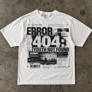 May include: A white short-sleeved t-shirt featuring a large black graphic print on the front. The design includes the text ERROR 404: YOUTH NOT FOUND, along with various technical data, a barcode, a cityscape silhouette, and Japanese characters.