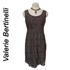 May include: A brown sleeveless dress with a lace pattern. The dress has a round neckline and a fitted bodice. The dress is on a mannequin and has a red beaded necklace.