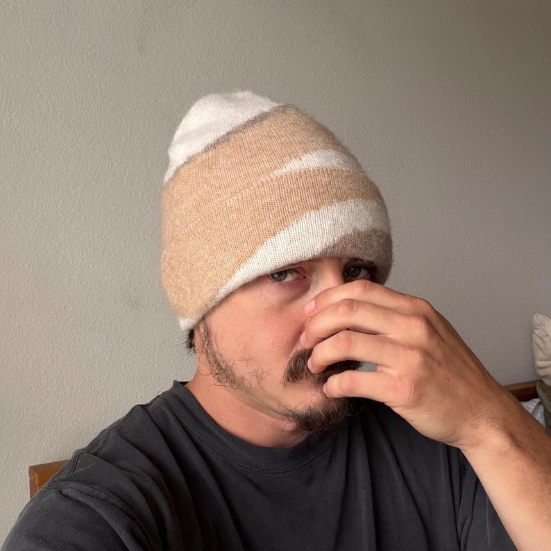 May include: A beige, white, and tan striped beanie hat. The hat is made of a soft, knitted material. The hat is worn by a person.
