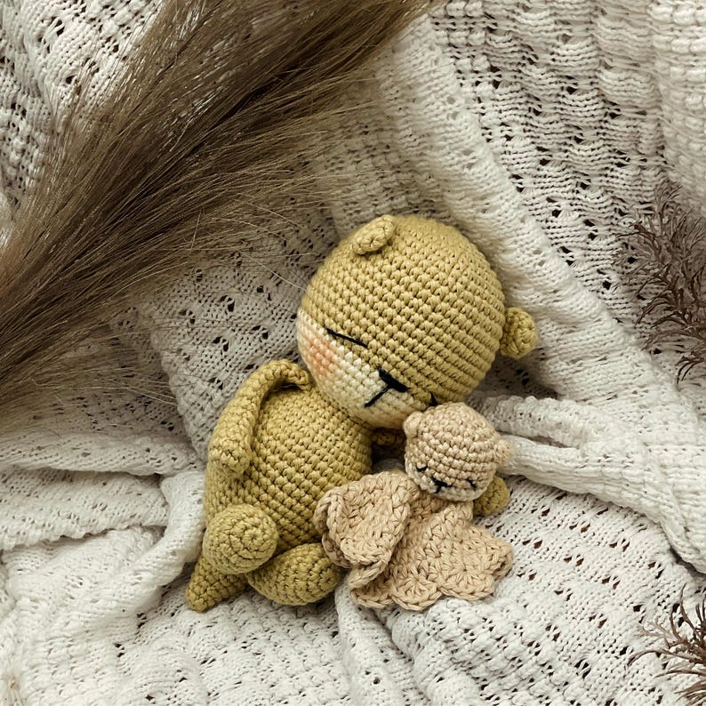 May include: Three crocheted toys: a large tan bear, a smaller tan bear, and a tan bunny. The bear's face has black and pink details. The toys are on a white, textured blanket.