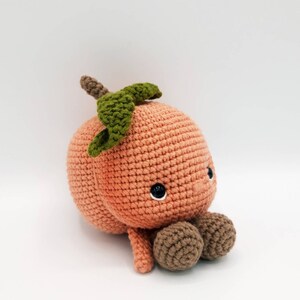 May include: A crocheted peach plush toy with a green leaf on top and brown crocheted feet. The peach has a cute face with black eyes.