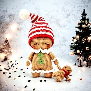 Op de afbeelding: Twee gehaakte gingerbread-poppetjes, een grote en een kleine, met rood-wit gestreepte mutsen. De grotere gingerbread staat met zijn ogen dicht, terwijl de kleinere gingerbread ligt. Beide bevinden zich op een wit oppervlak met zwarte stervormige confetti.
