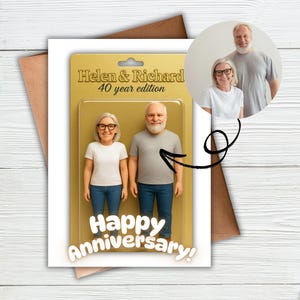 May include: A greeting card featuring a 3D figurine set of a couple, labelled "Helen & Richard 40 year edition." The card also has a photo of the couple and the words "Happy Anniversary!" The card is on a white surface.