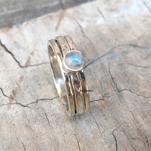 May include: A silver ring with a moonstone set in the centre. The ring has three bands that are stacked on top of each other.